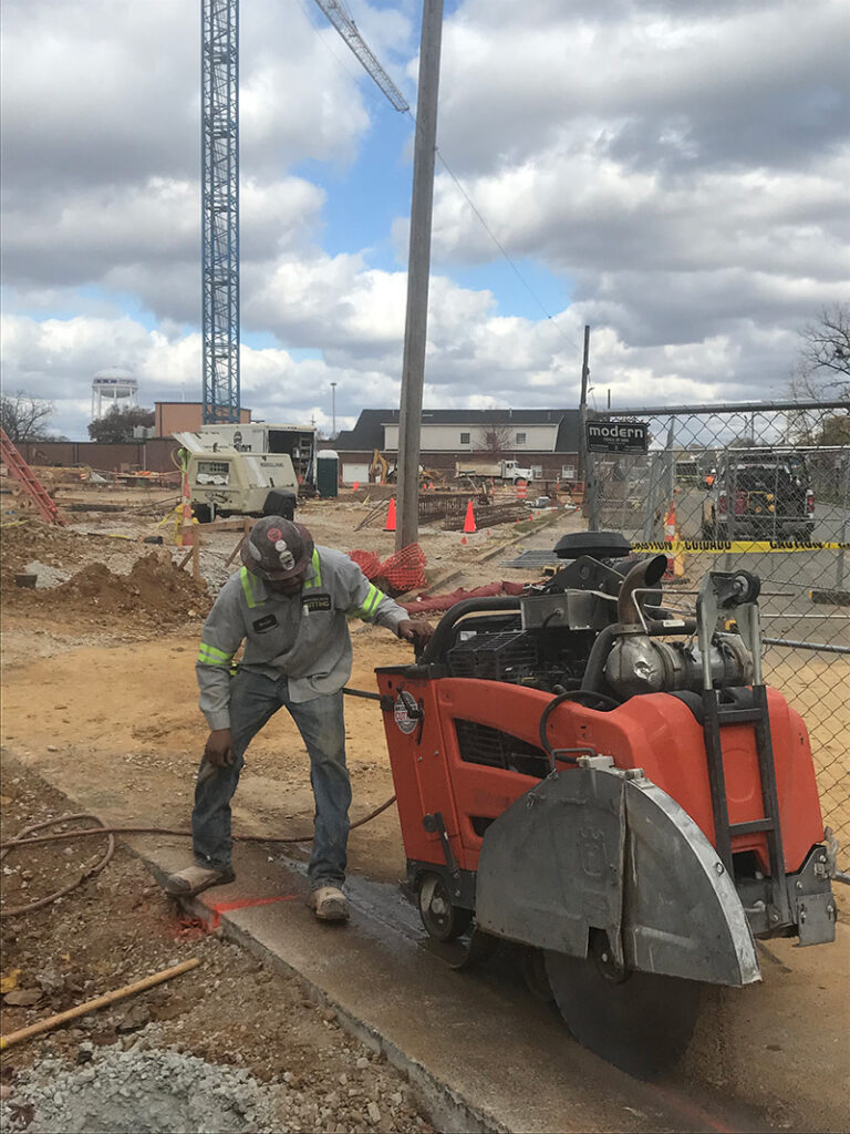 Image of an Any Concrete Cutting technician using large equipment to cut a concrete slab on the ground outside.