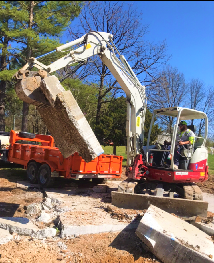 An Any Concrete Cutting technician lifting a concrete slab using a backhoe for an outside demolition service
